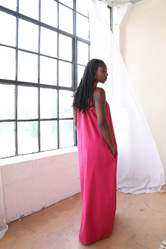 Woman in a pink dress standing in a room with large windows and white walls.